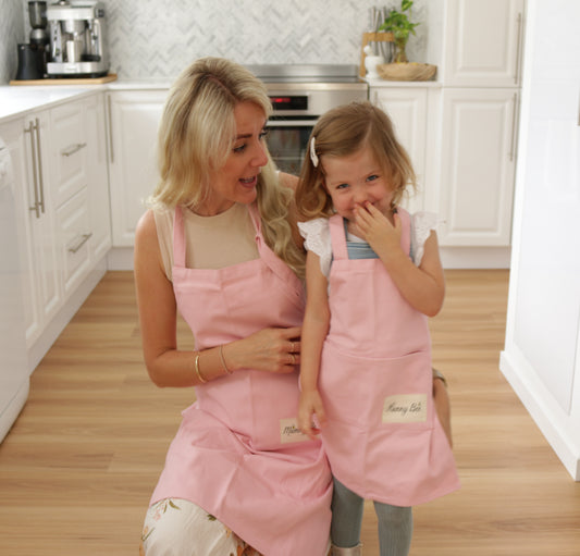 Mother and Daughter wearing matching pink apron set, mother's apron has Mummy bee print and Girl's apron has Hunny bee print, 100% organic cotton