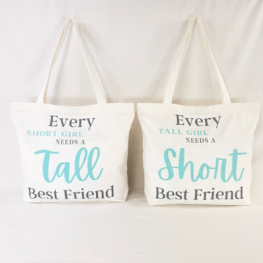 Tall Friend and Short Friend bags, one bag print text reads : "Every Short girl needs a tall best friend" and the words "short girl" and "Tall" is in Teal color and rest of writing is in dark grey. the other bag print reads: "Every tall girl needs a short best friend" colouring of the print text is the same as the other bag.  Bag itself is white with shoulder straps, zipper on the top